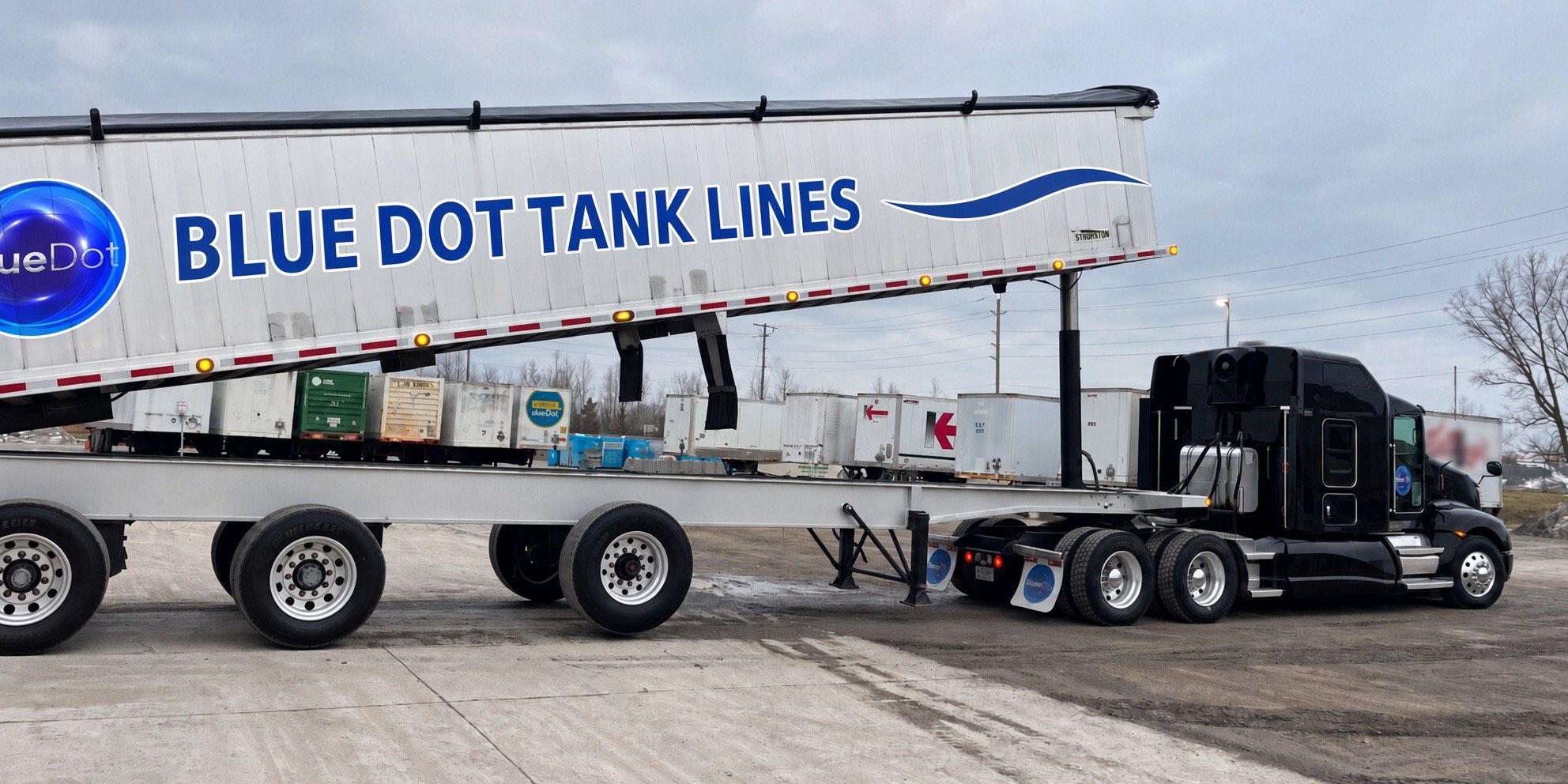 Blue Dot Tank Lines end dump trailer raised for unloading, hooked to a black tractor