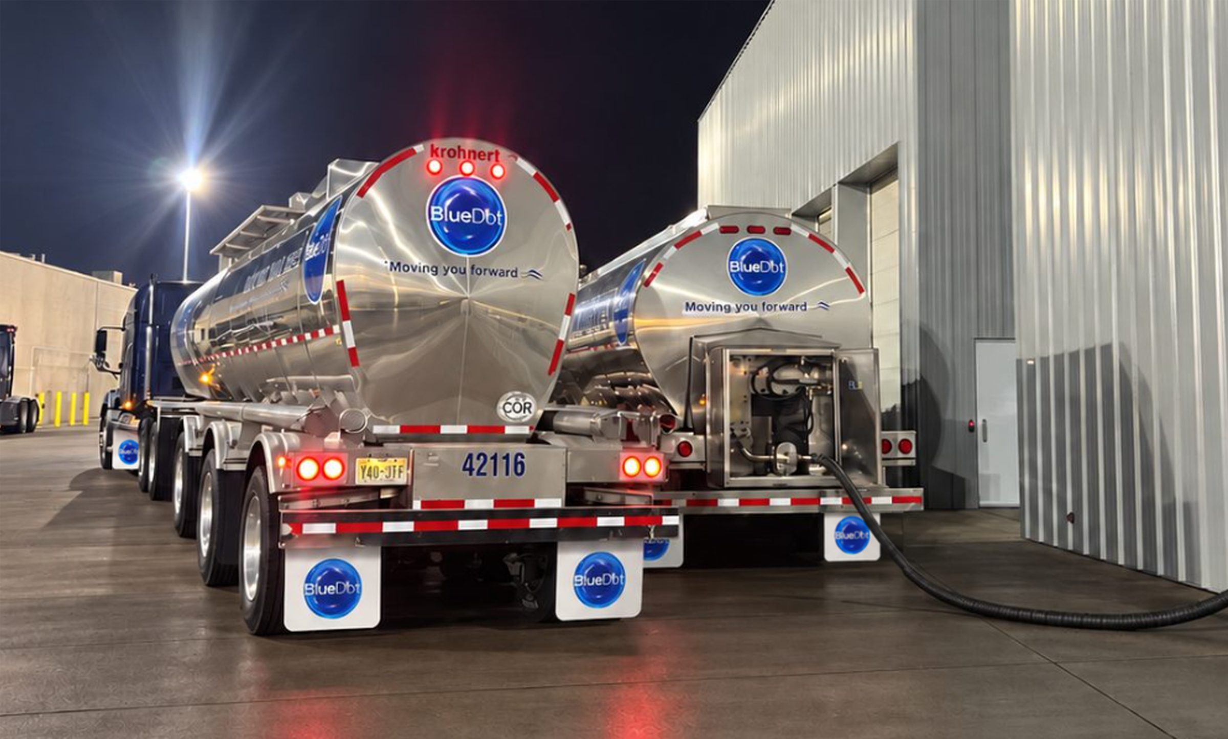 Two Blue Dot stainless food-grade tank trailers loading at a facility at night